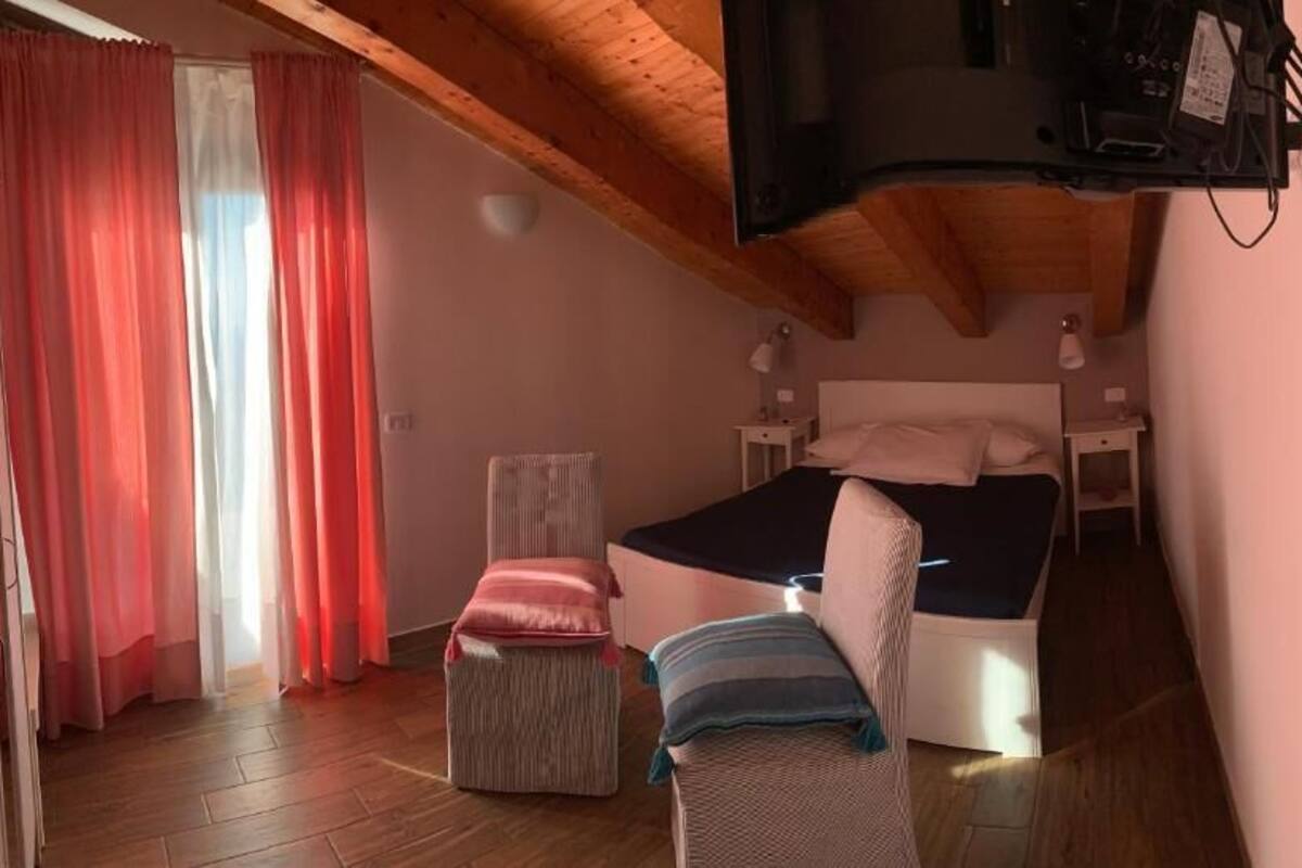 Une chambre à coucher comprenant un lit, une chaise, une petite table et un téléviseur fixé au mur.