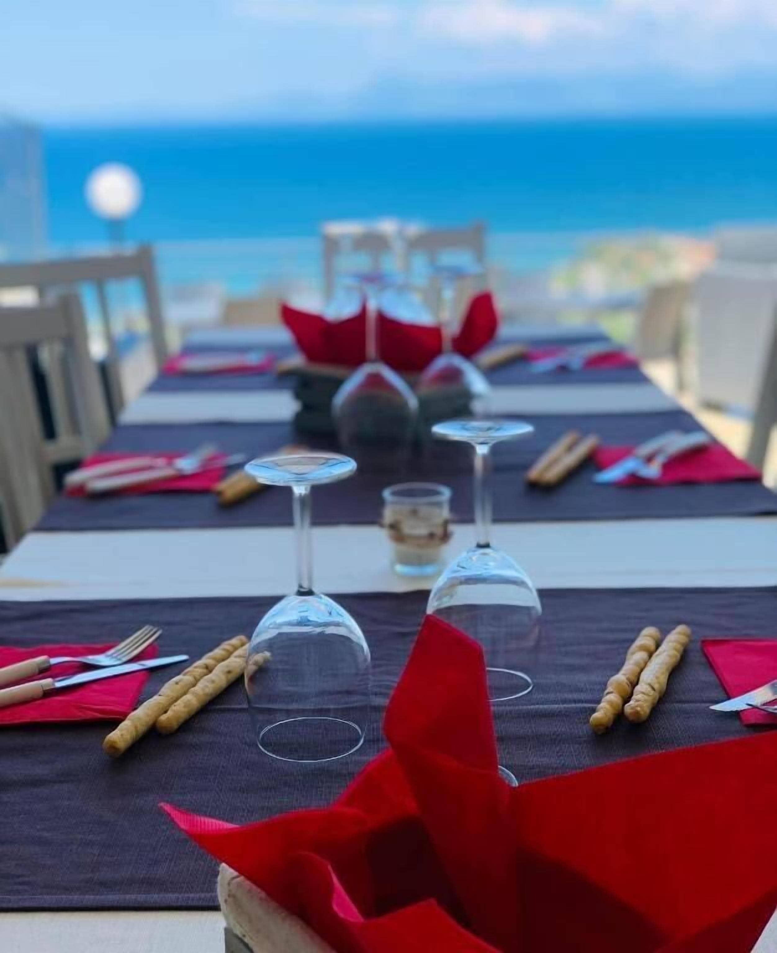 A table set for dining with wine glasses, cutlery, and bread rolls, overlooking a body of water.