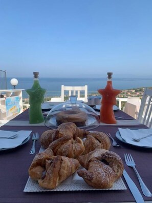 A table with croissants, a glass dome, and two decorative bottles, overlooking a scenic view. - B&B STELLA DEL CILENTO ROOMS (Agropoli)