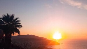 Ένα ηλιοβασίλεμα πάνω από ένα παράκτιο τοπίο με κτίρια και φοίνικες.