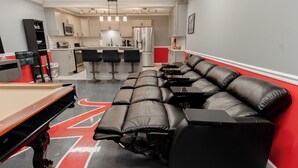 Un salon moderne avec une table de billard, un canapé et un coin cuisine à l’arrière-plan.