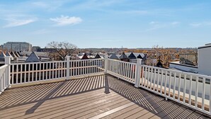 Una terrassa de fusta amb baranes blanques, amb vista a un paisatge urbà ple d'edificis i terrats.