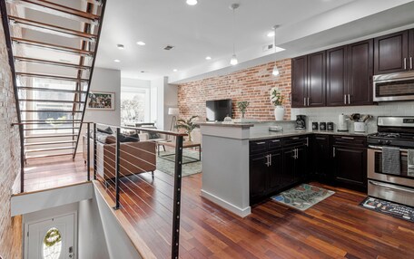 A modern kitchen with dark wooden cabinets, a brick accent wall, and a stainless steel oven.