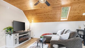 A modern living room with a wooden ceiling, a flat-screen TV, a sofa, and a small table with a plant.