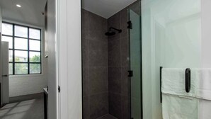 A modern bathroom with a glass shower enclosure, a white towel rack, and a large window providing natural light. - Wow! Luxury inner-city two bedroom apartment (Dunedin)