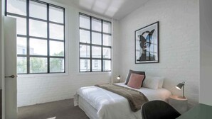 A bedroom with a bed, a desk, a chair, a lamp, and a framed picture on the wall. - Wow! Luxury inner-city two bedroom apartment (Dunedin)