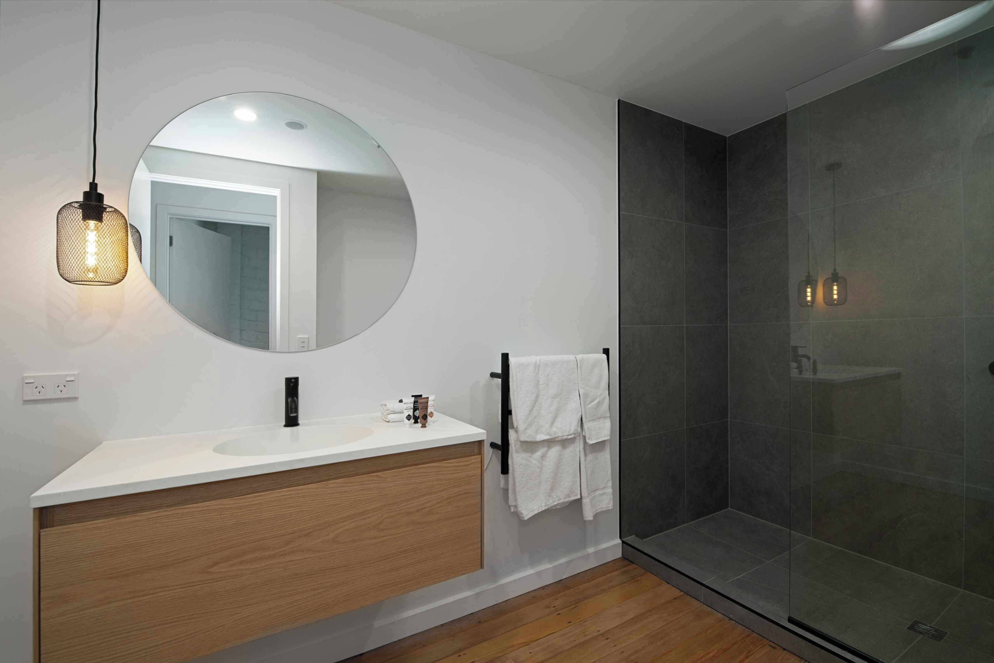 A modern bathroom with a white vanity, a round mirror, and a glass-enclosed shower.