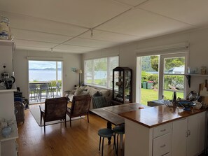 A spacious kitchen with a wooden countertop, a dining area with chairs, a sofa, and a view of a lake through large windows.