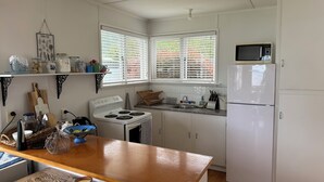 A compact kitchen with white appliances, a wooden countertop, and a window with blinds. - Lake Rotoiti Lakefront Bach with Stunning Sunsets (Rotoiti Forest)