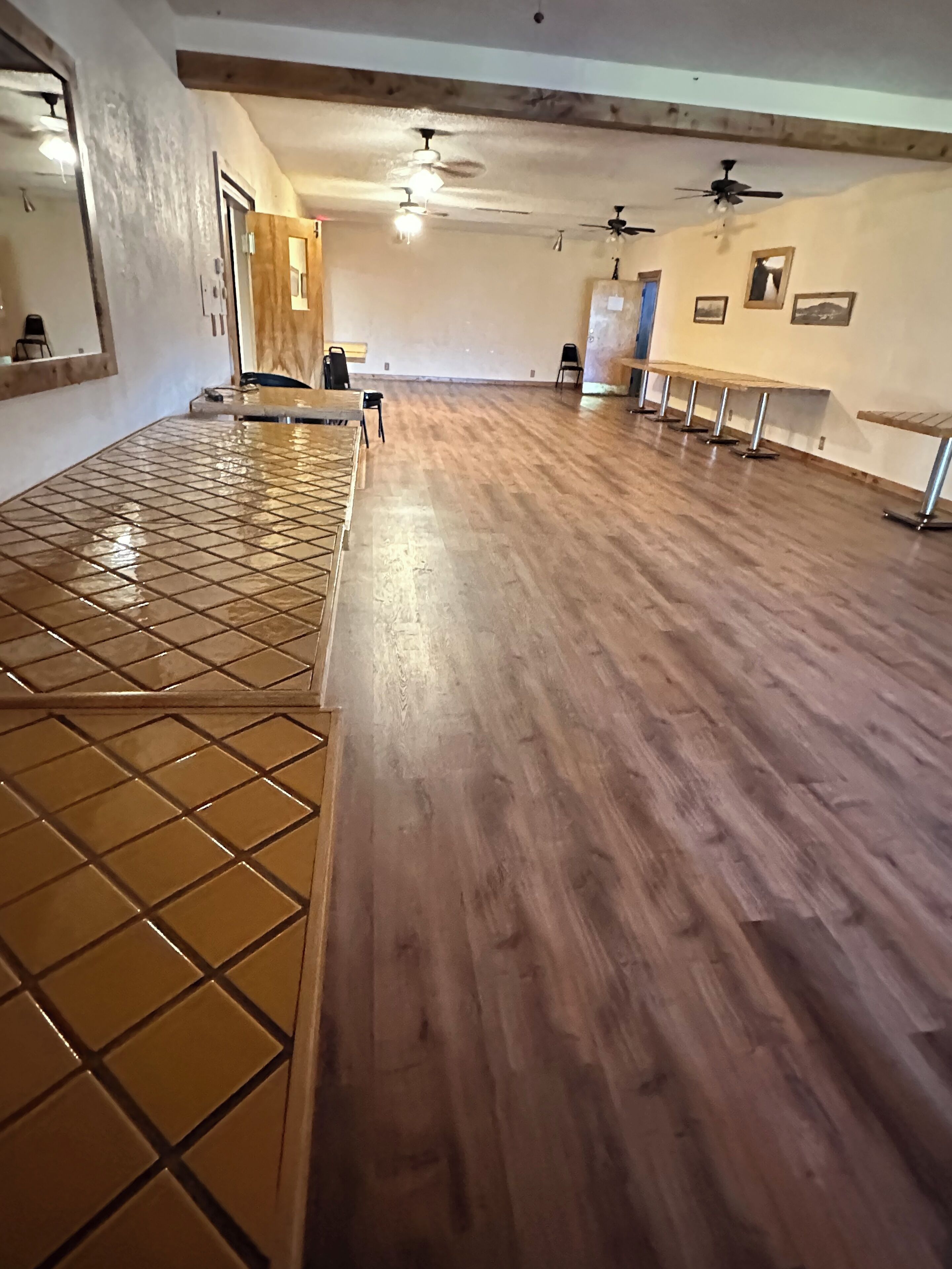 A spacious room with a wooden floor, a tiled area, and ceiling fans.