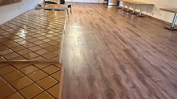 Ein geräumiges Zimmer mit Holzboden, gefliestem Bereich und Deckenventilatoren.