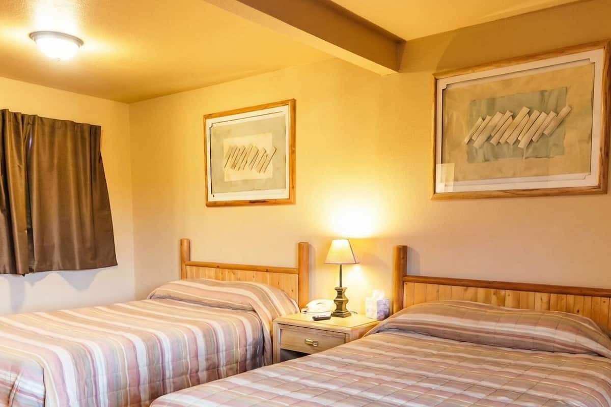 Camera d'albergo con due letti, un comodino con una lampada, un quadro appeso alla parete e una finestra con tende.