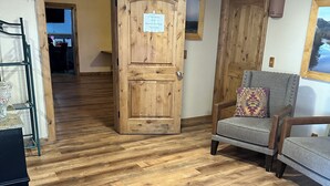 A room with wooden flooring, a wooden door with a sign, a grey armchair, and a wooden cabinet. - General Kearny Inn (Kearny)