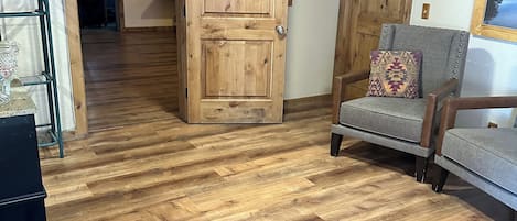 A room with wooden flooring, a wooden door with a sign, a grey armchair, and a wooden cabinet.
