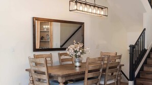Una sala menjador amb una taula de fusta, sis caires, un ram de flors, un mirall gran i una escala amb barana negra.