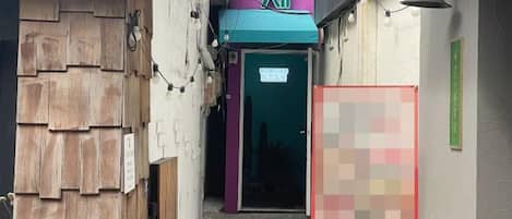 A narrow alleyway with a wooden structure on the left and a building entrance with a green awning on the right.