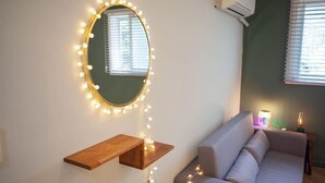 A room with a round mirror with lights, a wooden shelf, a sofa, and a window with blinds. - Mihojae Seomyeon (Busan)