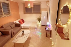 Un ambiente compatto con divano, letto, un piccolo tavolo e uno specchio con illuminazione.