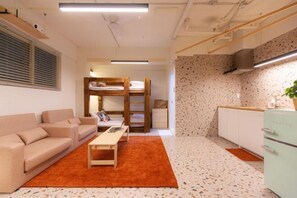 Un ambiente compatto con un divano, un tavolino, un letto a castello e angolo cottura.