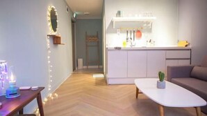 A modern living room with a wooden floor, a white sofa, a white coffee table, and a kitchen area with a white countertop and cabinets. - Mihojae Seomyeon (Busan)