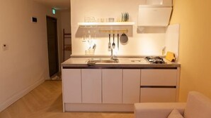 A compact kitchen with white cabinets, a countertop, and hanging utensils. - Mihojae Seomyeon (Busan)