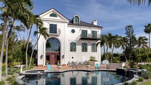 Une grande maison à deux étages avec une piscine, entourée de palmiers et d’une pelouse bien entretenue.