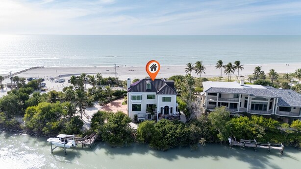 Une propriété située en bord de mer, comprenant une grande maison et un bâtiment plus petit, le tout entouré d’une végétation luxuriante et doté d’un quai pour bateaux.