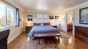 A bedroom with a large bed, a bedside table, a lamp, and a view of the outdoors through a window. - Charming Fort Bragg Home with Ping-Pong & Fire Pit (Fort Bragg)