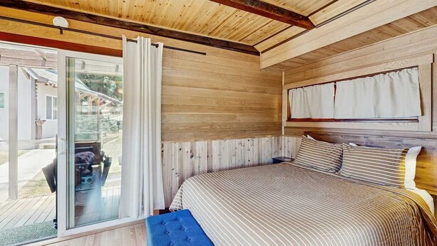 A bedroom with a bed, a bench, a sliding glass door, and a window. - Eco-Conscious Home with Spacious Yard & EV Charger (Fort Bragg)