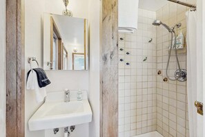 A bathroom with a sink, mirror, and shower. - Eco-Conscious Home with Spacious Yard & EV Charger (Fort Bragg)