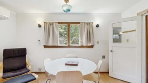 A room with a round table, two chairs, a sofa, a window with curtains, a ceiling light, and a door. - Eco-Conscious Home with Spacious Yard & EV Charger (Fort Bragg)