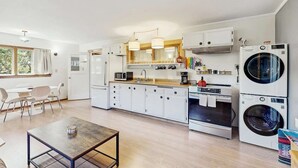 A modern kitchen with white cabinets, a dining area with a table and chairs, and a laundry area with stacked washing machines. - Eco-Conscious Home with Spacious Yard & EV Charger (Fort Bragg)