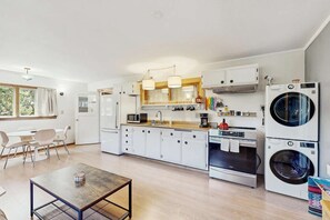 A modern kitchen with white cabinets, a dining area with a table and chairs, and a laundry area with stacked washing machines. - Eco-Conscious Home with Spacious Yard & EV Charger (Fort Bragg)