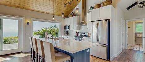 A modern kitchen with a large island, wooden ceiling, and large windows.