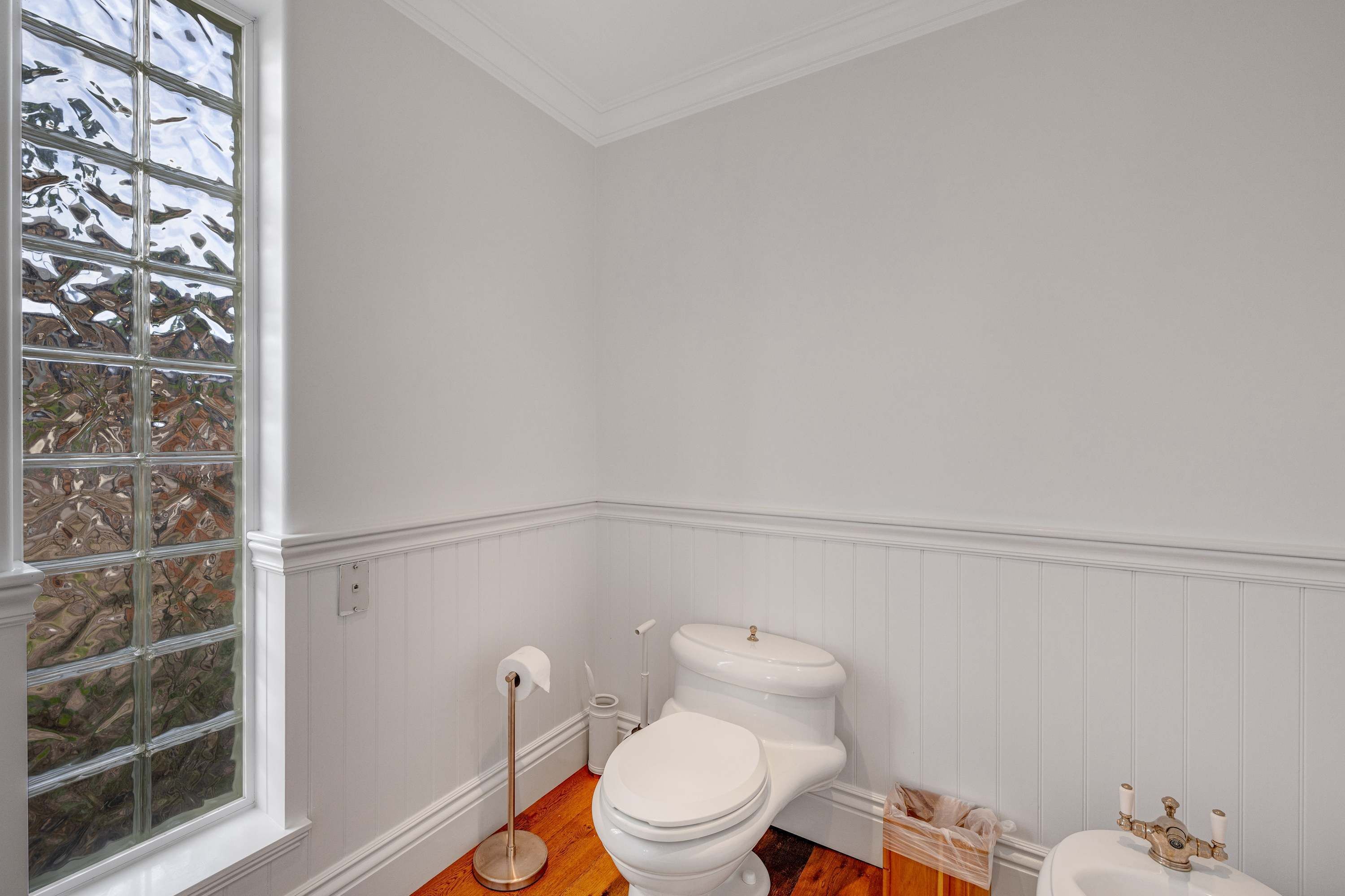 A bathroom with a white toilet, a bidet, a small sink with a gold faucet, and a window with a view of trees.