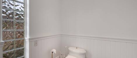 A bathroom with a white toilet, a bidet, a small sink with a gold faucet, and a window with a view of trees.