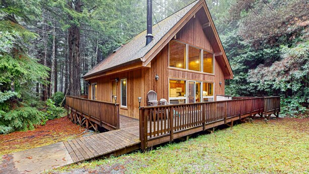 Une cabane en bois dotée d’une terrasse, de grandes fenêtres et d’une cheminée.