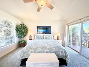 A bedroom with a bed, a ceiling fan, a large window, a TV, and a potted plant. - Oceanview Home with Hot Tub & Private Beach Access (Fort Bragg)