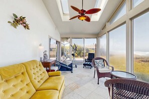 A spacious room with a yellow sofa, a ceiling fan, a treadmill, and a view of the outdoors. - Oceanview Home with Hot Tub & Private Beach Access (Fort Bragg)