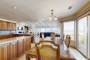 A spacious kitchen with wooden cabinets, a dining area with a large table and chairs, and a view of the beach through large windows. - Oceanview Home with Hot Tub & Private Beach Access (Fort Bragg)