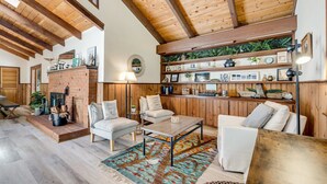 A spacious living room with a brick fireplace, wooden ceiling beams, and a cozy seating area with a coffee table and chairs. - Family Getaway - Hot Tub, Fire Pit & Dog Friendly (Mendocino)
