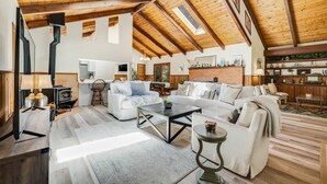 A spacious living area with high ceilings, a fireplace, and a kitchen in the background. - Family Getaway - Hot Tub, Fire Pit & Dog Friendly (Mendocino)