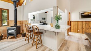 A kitchen with a central island, wooden chairs, a stove, and a large window. - Family Getaway - Hot Tub, Fire Pit & Dog Friendly (Mendocino)