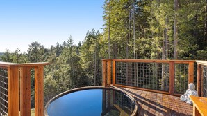 Eine Holzterrasse mit einem runden Whirlpool, umgeben von einem Wald.