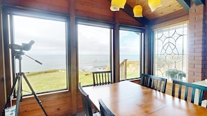 A room with large windows offering a view of the ocean, a telescope on a tripod, and a wooden table with chairs. - Tideaway Private Hot Tub and Expansive Ocean View (Fort Bragg)