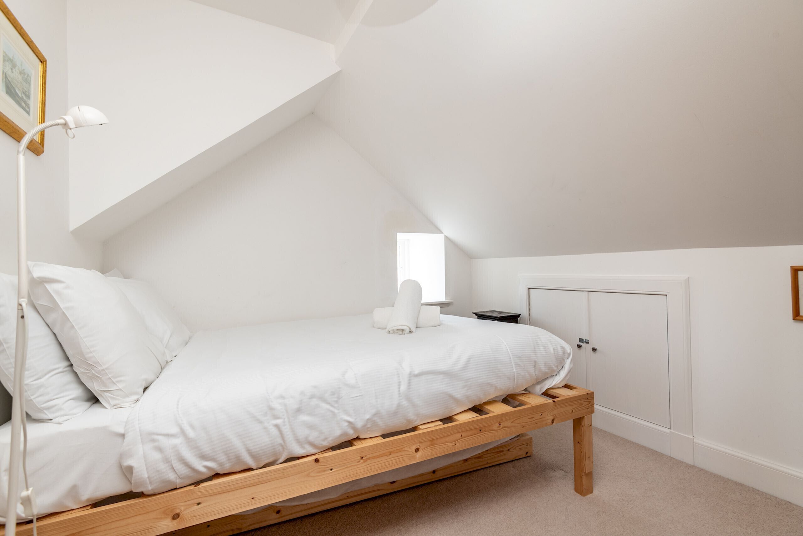 A single bed with a wooden frame in a room with white walls and a sloped ceiling.