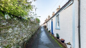 A narrow street with white houses, blue doors, and potted plants along the sidewalk. - Ve-Marn Cottage | Kilrenny (Kilrenny)
