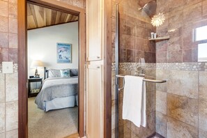 A bathroom with a shower, a towel rack, and a bed visible in the adjacent room. - Oceanfront Sanctuary - Private Cove, Deck, Grill (Fort Bragg)