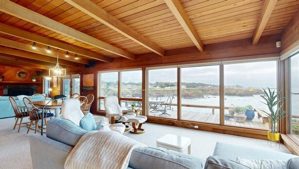 A spacious living room with a large wooden ceiling, a cozy seating area, and a view of the coastline through large windows. - Oceanfront Haven with Beach Access, Views & Deck (Fort Bragg)