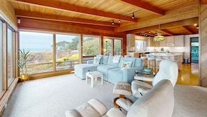 A spacious living room with a large sectional sofa, a glass coffee table, and a view of the outdoors. - Oceanfront Haven with Beach Access, Views & Deck (Fort Bragg)